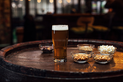 Close up shot of beer and snacks (peanuts, popcorn) on the barrel table in a pub
