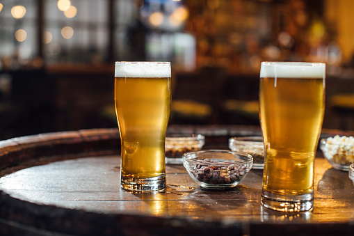 Glasses of Beer and Peanuts on a Wooden Table at a Pub, a Close Up