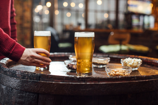 An unrecognizable man's hand holding a glass of craft beer at a bar