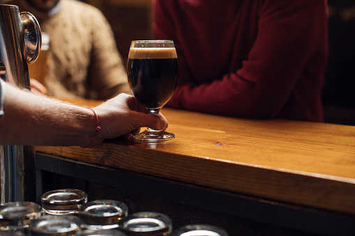 Unrecognizable bartender holding a pint of cold Guinness ready to be served