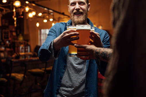 Happy hour at the bar: smiling man bringing beer for his mates
