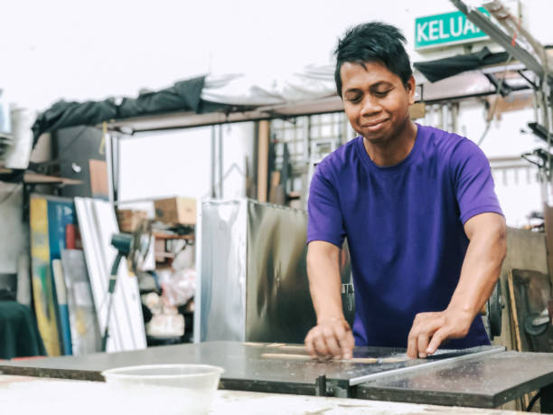 Asian malay smiling male worker cutting acrylic with machine at signboard workshop stock photo