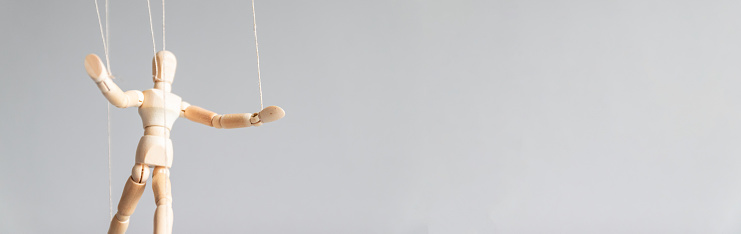 Wooden puppet doll on the clothesline on a gray background with copy space. Human control concept.
