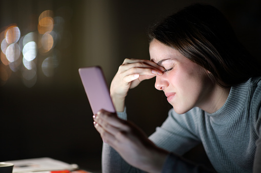 Tired woman suffering eyestrain using phone in the night