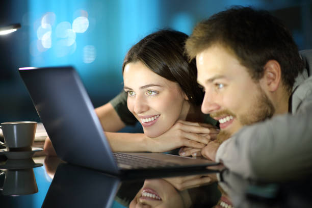 happy couple watching media on laptop in the night - gamer watching tv adult couple imagens e fotografias de stock