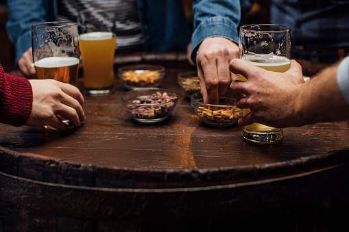 Hands of anonymous young men drinking beer and eating peanuts at the pub