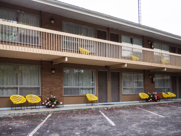 Exterior view of a motel in summer with a fence on the second floor and yellow chairs