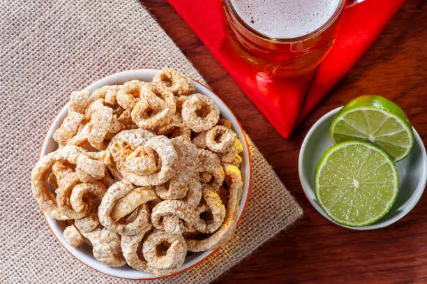 Photo of Crackling in a bowl. Accompanied by lemon and a glass of beer. Boteco food, typical in Brazil.