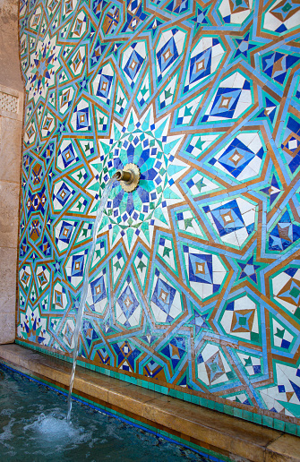Fragment of the ablution fountain decorated with mosaic tiles with traditional geometric patterns in front of the Mosque Hassan II in Casablanca, Morocco. Blurry motion of flowing water