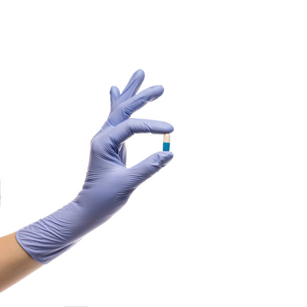 main dans le gant de latex avec une pillule dans une capsule sur un fond blanc - surgical glove human hand holding capsule photos et images de collection