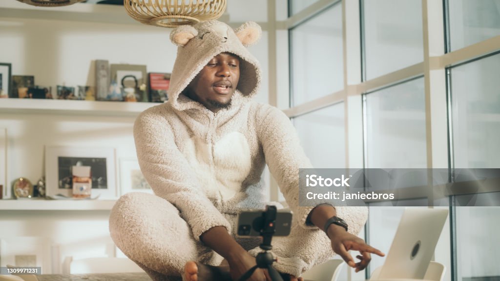 Missing a friend during lockdown. African man doing video call in cute bear onesie. Using smart phone Online meeting during pandemic. Young man enjoying online date in cute outfit Union Suit Stock Photo