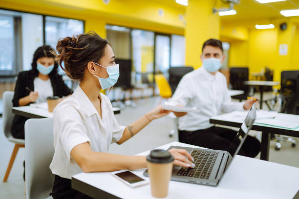 istock Office worker wearing medical face mask for social distancing  for virus prevention while using laptop back at work in office. 1309971343