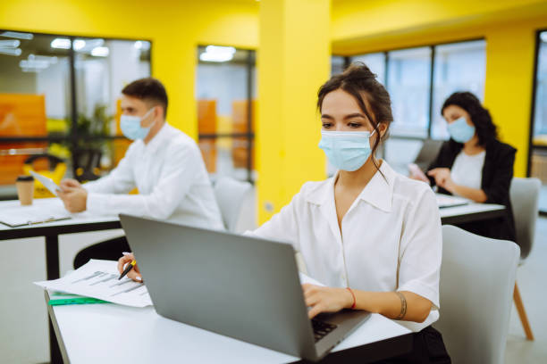 istock Office worker wearing medical face mask for social distancing  for virus prevention while using laptop back at work in office. 1309971351