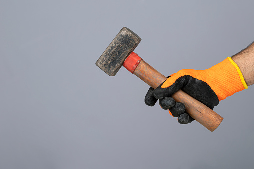 Manual worker holding a hammer in his hand. Isolated on a gray background.