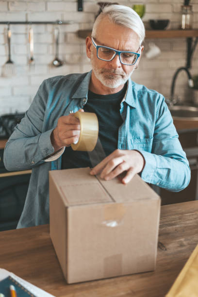 istock Send a parcel. An elderly man seals the box with duct tape 1309975130