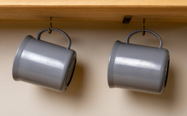 istock Two gray colored mugs hanging from two hooks under a wooden stand on a white background. Used for morning or afternoon coffee or tea. Casual disposition referring to family vacations. 1309975536