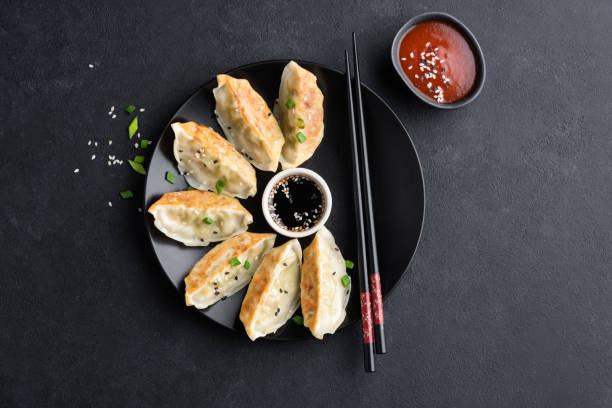 Asian food Gyoza or Jiaozi fried dumplings Asian food Gyoza or Jiaozi fried dumplings served with soy sauce, shriracha sauce and sesame seeds on black concrete background, top view chinese dumpling stock pictures, royalty-free photos & images