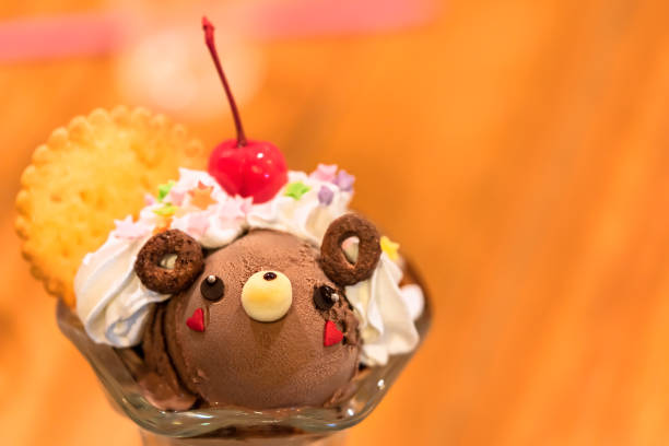 Japanese dessert in a stemware glass depicting ice cream shaped as a cute bear character in chocolate topped with sweet whipped cream, cookie and cherry fruit.
