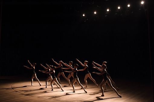 A choreographed dance of a group of graceful pretty young ballerinas practicing on stage in a classical ballet school