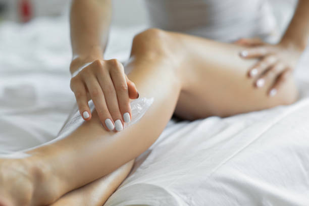 kvinna som applicerar kropps lotion på benen i sitt sovrum. - krämer bildbanksfoton och bilder