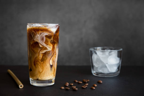 iced coffee in tall glass with cream, container with ice, cocktail straw and coffee beans on dark background with copy space. refreshing drink - pouring coffee liquid coffee bean imagens e fotografias de stock