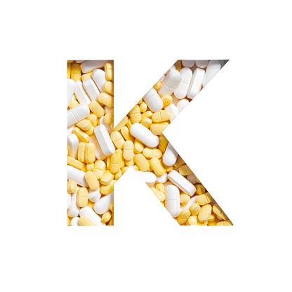 Letter K of English alphabet made of pills and paper cut isolated on white. Pharmacy typeface. High quality photo