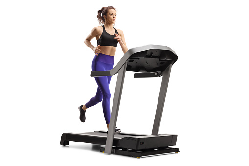 Young woman running on a treadmill machine isolated on white background