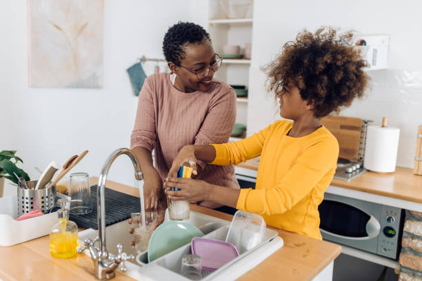 african american senior woman washing dishes with the help of her granddaughter - senior getting groomed studio imagens e fotografias de stock