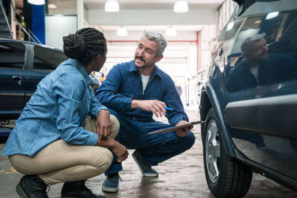 Car mechanic talking with customer Car mechanic checking car wheel in the auto repair shop, holding clipboard and talking with customer. repairman stock pictures, royalty-free photos & images