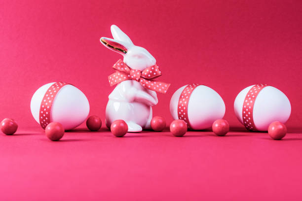 istock Porcelain rabbit with three white eggs decorated with pink ribbon on pink paper background. 1309995409