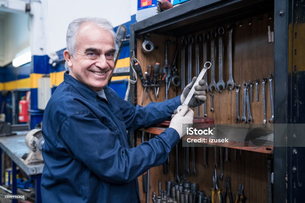 Senior car mechanic at work Auto mechanic holding wrench and smiling at camera. Active Seniors Stock Photo