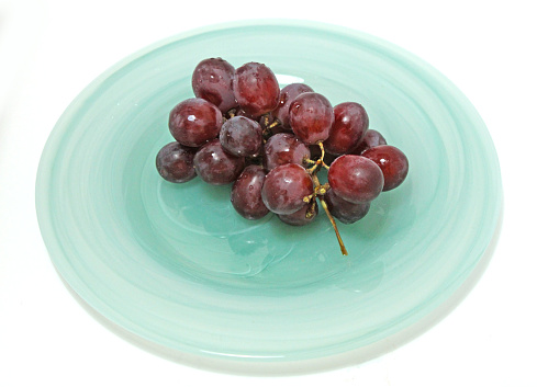 A bunch of red, seedless grapes on a swirled, mint-green glass plate with a white background.
