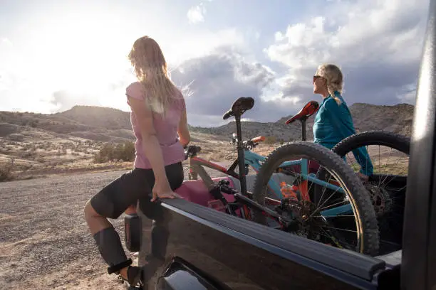 Photo of Female mountain bikers relax on bed of truck after a successful ride