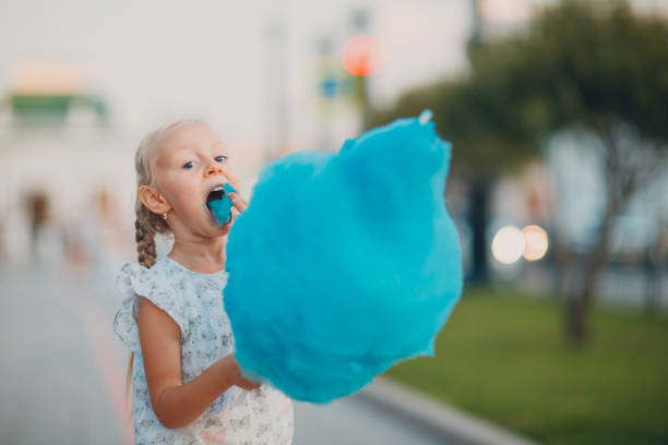 Little blond girl eating cotton candy and shows blue tongue in the park. Little blond girl eating cotton candy and shows blue tongue in the park child cotton candy stock pictures, royalty-free photos & images