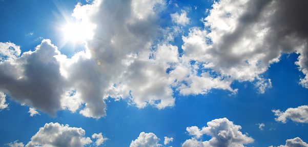 Beautiful, blue summer sky with fluffy clouds and bright sun as a background.