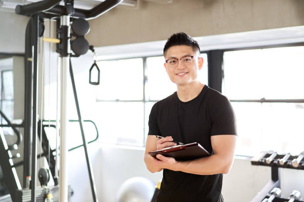 トレーニングジムで笑顔で立っているアジアの男性トレーナー - tutor ストックフォトと画像