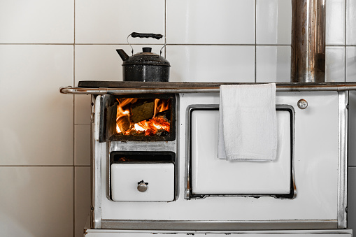 Image with fire flames inside a white wood burning stove and a black kettle
