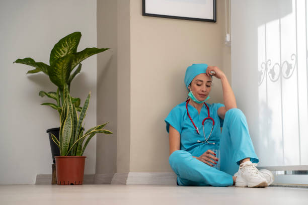 istock Overworked female medical professional wears face mask, blue uniform and gloves sits on hospital floor 1310020708