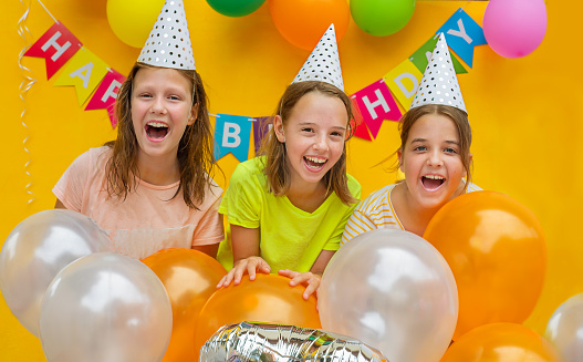 Three girls with balloons on a yellow background. Children at the birthday party