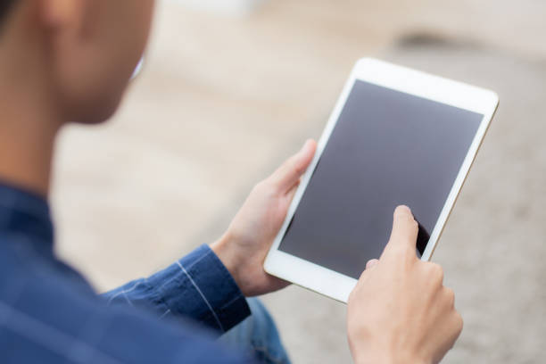 istock Closeup young asian man sitting and using mockup of tablet computer with display blank screen on sofa at home, male holding digital tablet watch entertainment at living room, communication concept. 1310025623