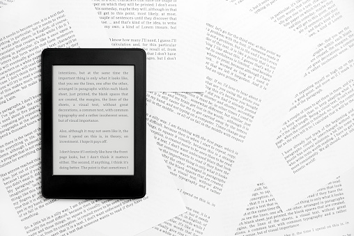Electronic reader with the screen on and a text on it, on sheets of paper with text printed on them. Concepts: reading and digital technology. Flat lay image with copy space.