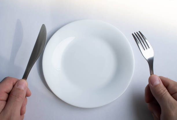 istock Fork and knife in hand against the background of an empty plate. 1310029483
