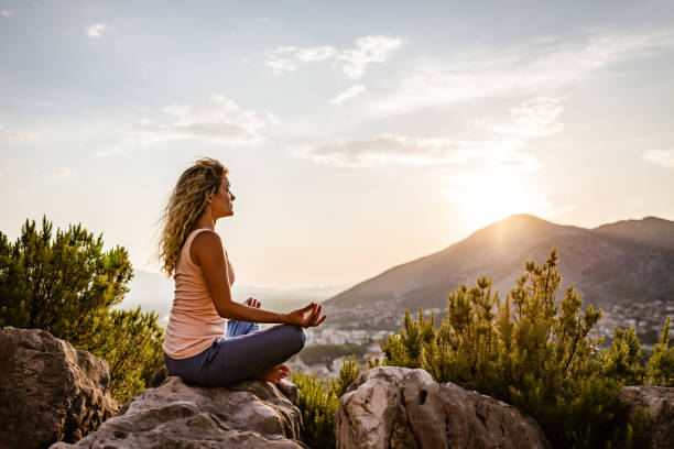 young woman preforms yoga in mountains at sunset - zen like nature breathing exercise sitting imagens e fotografias de stock