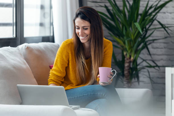 istock Confident young woman working with her laptop while drinking a cup of coffee sitting on a couch at home 1310046769