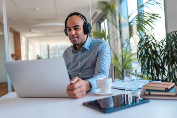 Smiling Mixed Race Male in 40's Online Education Conference Call Front view of a smiling mixed race male in mid 40's taking a part of an online educational program. Sitting comfortably in his dining using his laptop. Online education conference call. one mature man only audio stock pictures, royalty-free photos & images