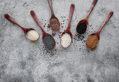 Wooden spoons with various healthy seeds and spices on gray concrete background