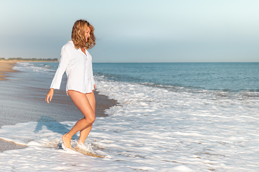 Mature woman on the beach on a summer's day getting her feet wet as she enters the water