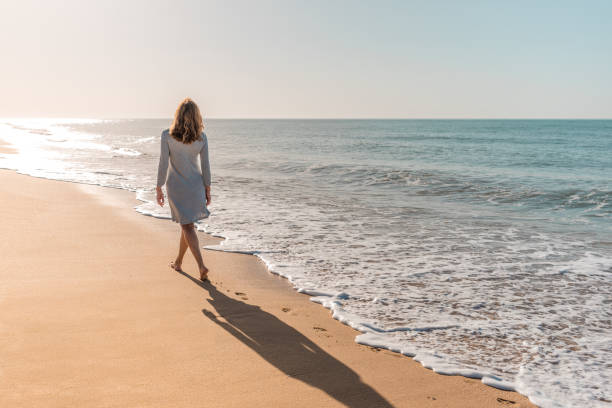 mujer caminando en la playa mirando al sol - one person beautiful barefoot beach fotografías e imágenes de stock