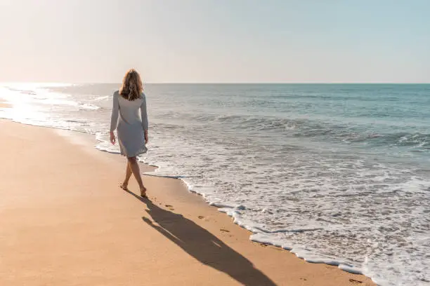 Photo of Woman walking on the beach looking at the sun