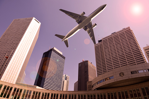 Low angle view of airplane flying over a skyscrapers at dusk with sunlight.